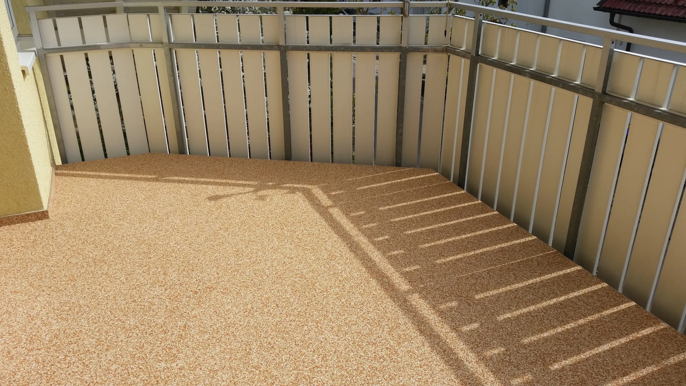 Beiger Steinteppich auf einem Balkon mit Holzgeländer